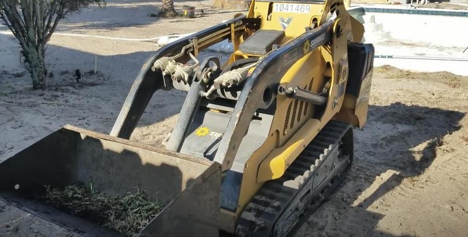 Small skid steer with grass-filled bucket.