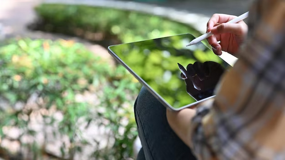 Person using a tablet with a stylus in a green landscape